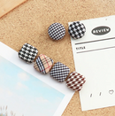 Dekorative knappenåle i stof på korktavle, runde og firkantede, forskellige mønstre og farver.