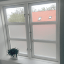 Vindue med sandblæst folie, der lukker lys ind. Pottet plante på vindueskarm.