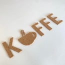 Bogstaverne "KOFFEE" i kork, med en kaffekop som "A", på en lys overflade.