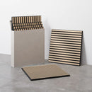 Akustikpaneler med striber i lys og mørk, kvadratisk form, lænet mod væg og i kasse.