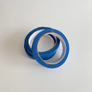 Tre ruller blå malertape med smal bredde ligger på en lys overflade.