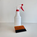 Hvid sprayflaske med rødt håndtag og skraber med orange greb og sort kant på lys baggrund.