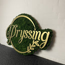 Dekorativ vægpynt med "Pryssing" i kursiv og bladdesign på grøn baggrund.