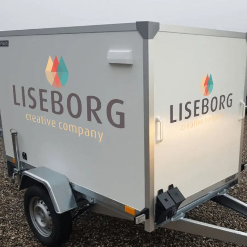 Trailer med "LISEBORG creative company" tekst og farverigt logo på grusunderlag.