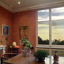 Stue med stor vindue, mønstret film, kunst på væggene, planter på bordet, lys filtreres blødt.