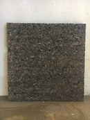 Mørk, kvadratisk plade med ujævn tekstur mod en enkel væg.