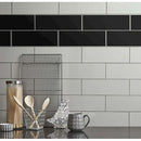 Flisevæg med grå og sorte fliser, træskeer i glas, metalrist og mønstret krus.