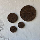 Fire mørke korkcirkler i varierende størrelser monteret på en hvid væg i et ikke-ensartet mønster.