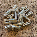 Små træclips med metalnål på korkoverflade, ligner miniature-tøjklemmer, flere i en bunke.