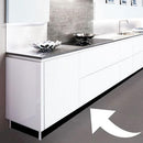 Moderne køkken med hvide skabe og sort sokkelfolie forneden; stor hvid pil peger på folien.