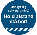 Blå cirkel med teksten "Beskyt dig selv og andre! Hold afstand stå her!" i hvid skrift.