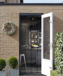 Sort dørforhæng i åben dør, udsigt til køkken, murstensvæg og krans, planter i forgrunden.