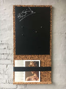 Opslagstavle med sort skrivetavle, magneter og en bred strimmel til magasiner eller aviser.