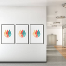 Tre indrammede plakater med geometriske mønstre i orange, teal og rød på en væg.