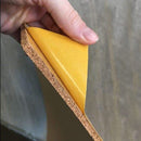 En hånd holder fleksibel kork med selvklæbende bagside, der er ved at blive pillet af.