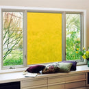 Vindue med gul folie, omgivet af planter og puder på vindueskarmen.