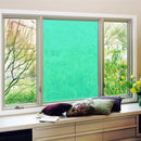 Vindue med tre ruder, midterste med turkis film. Puder og blomster på vindueskarmen.