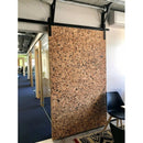 Stor, specklet korkpanel i døråbning, monteret på skinne. Stol og borddel synlige ved siden af.